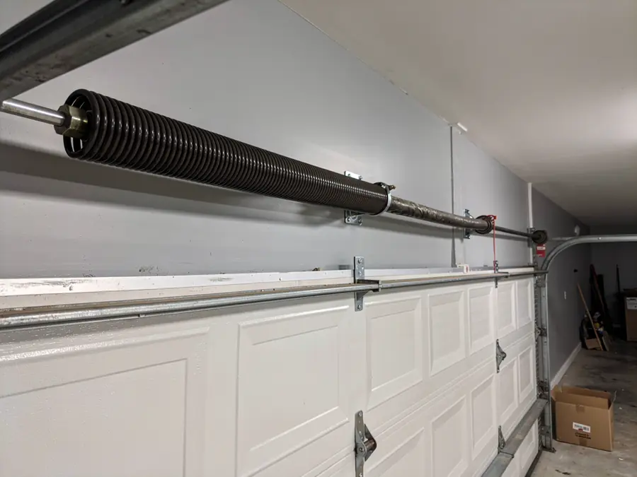 A garage door torsion spring is mounted above a white garage door.